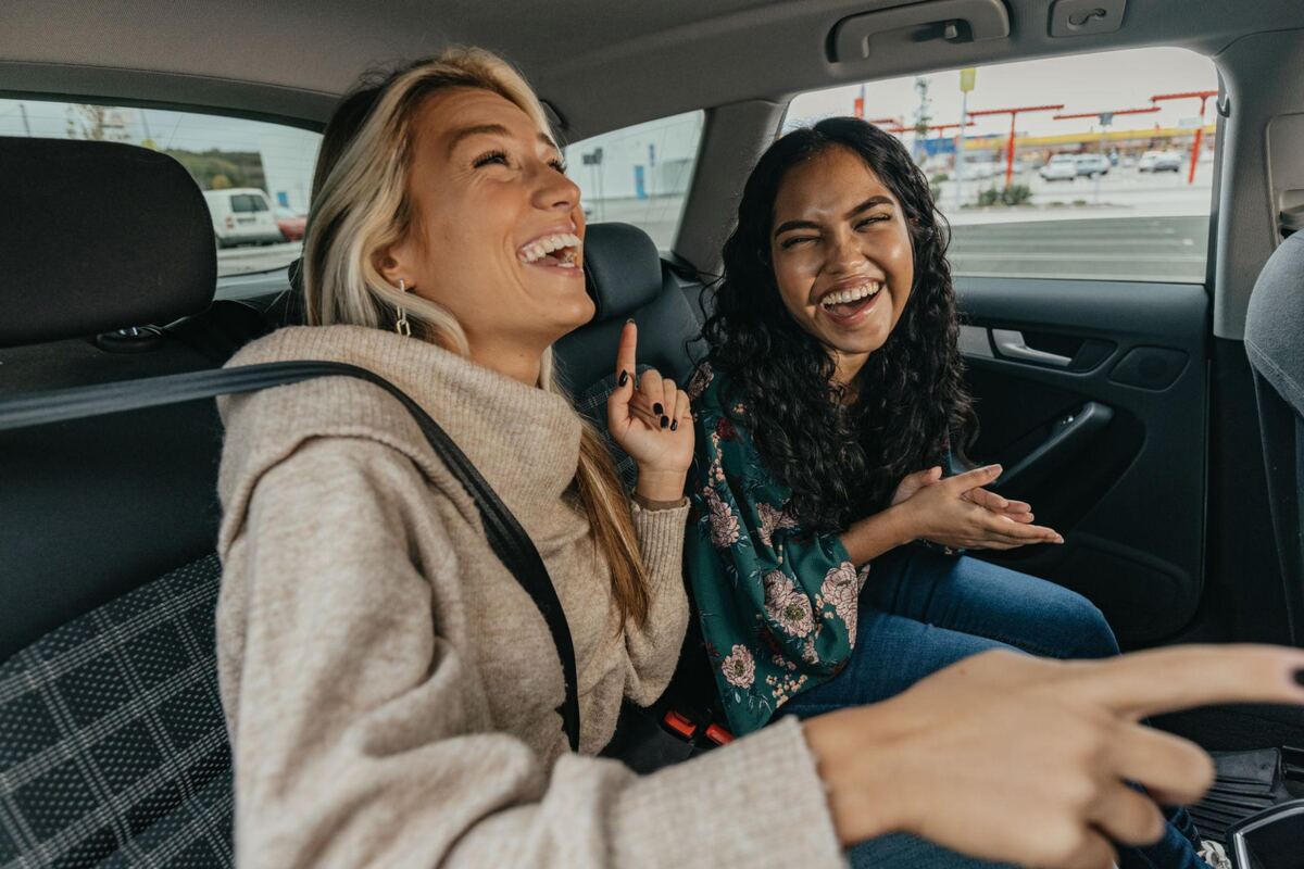 Two students laughing together in the back seat of a car